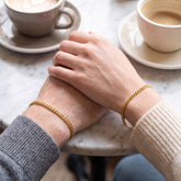 His & Hers gold Miami curb bracelets on a couple's wrists at a cafe table