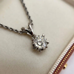 A close-up of a silver-toned necklace with a round-cut diamond pendant, resting on a cream-colored jewelry box.