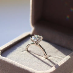 A radiant moissanite ring set in a polished pure silver band, encased in a charming grey velvet box, emphasizing the gem's prismatic sparkle