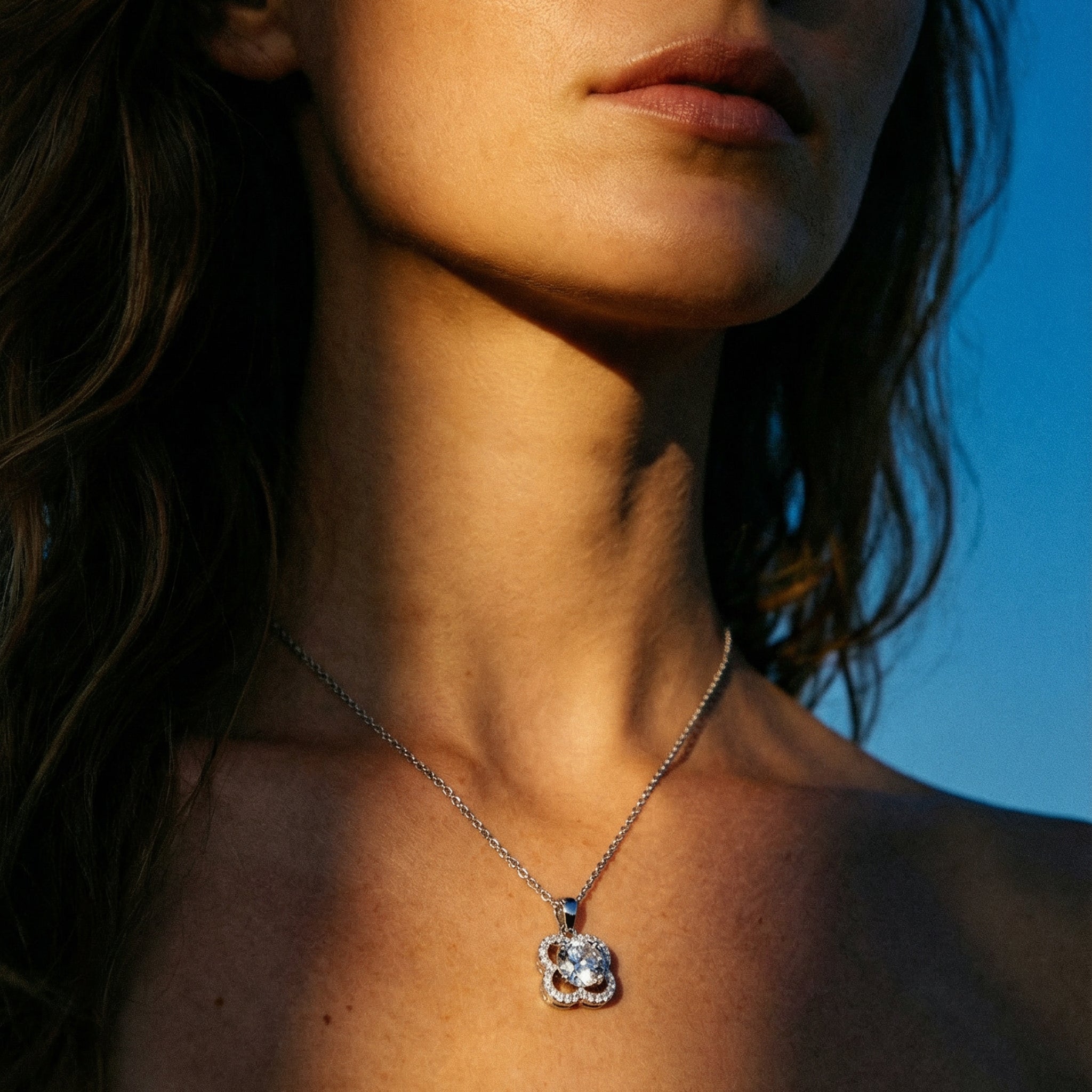 Close-up of a woman wearing a silver necklace with a pendant against a blue sky.