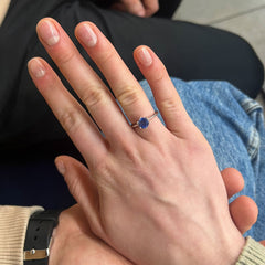 Hand wearing a ring with a blue gemstone, held by another person.