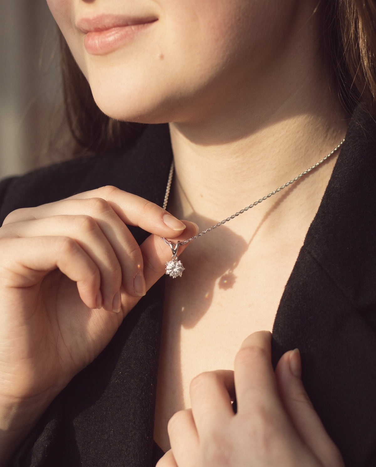Close-up of a moissanite pendant necklace resting on the collarbone, held between her fingertips