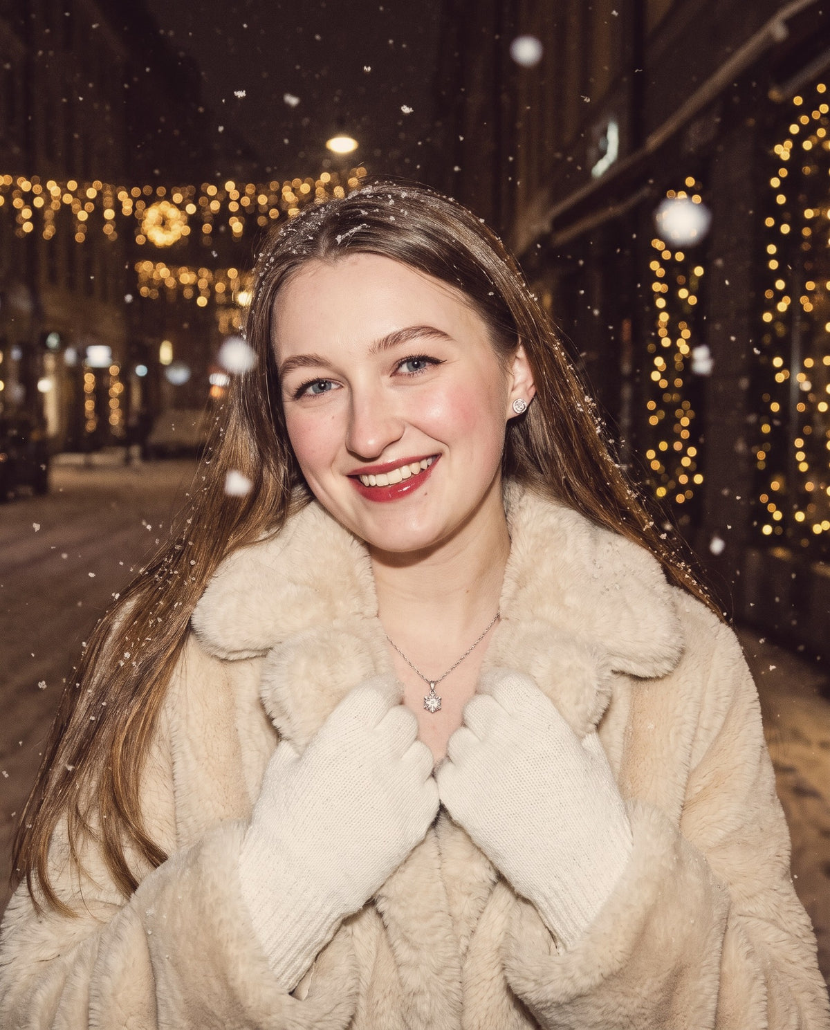 Woman smiling on a snowy evening street with festive lights, wearing a moissanite pendant necklace