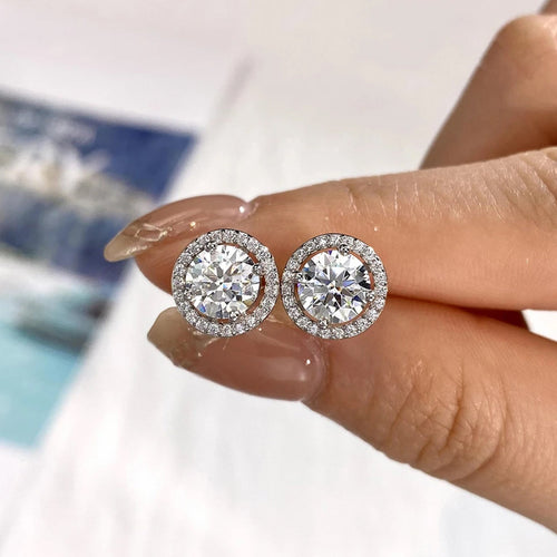 Halo moissanite stud earrings held between two fingers