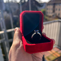 Red velvet box with a silver ring inside, held by a hand on a balcony.