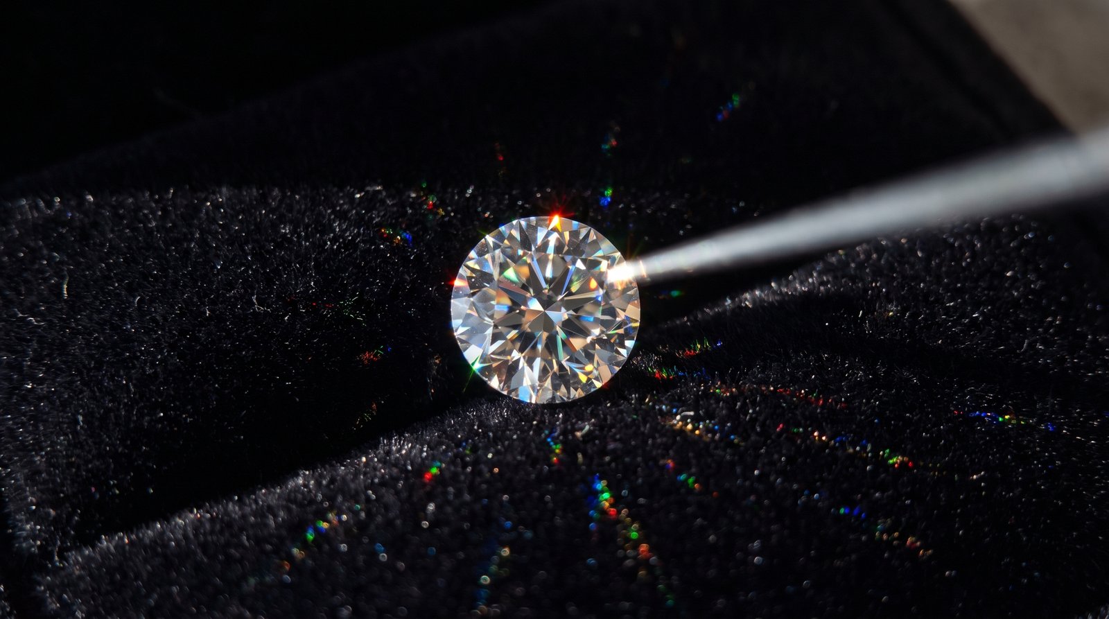 Round brilliant moissanite on black velvet throwing rainbow fire under a beam of light